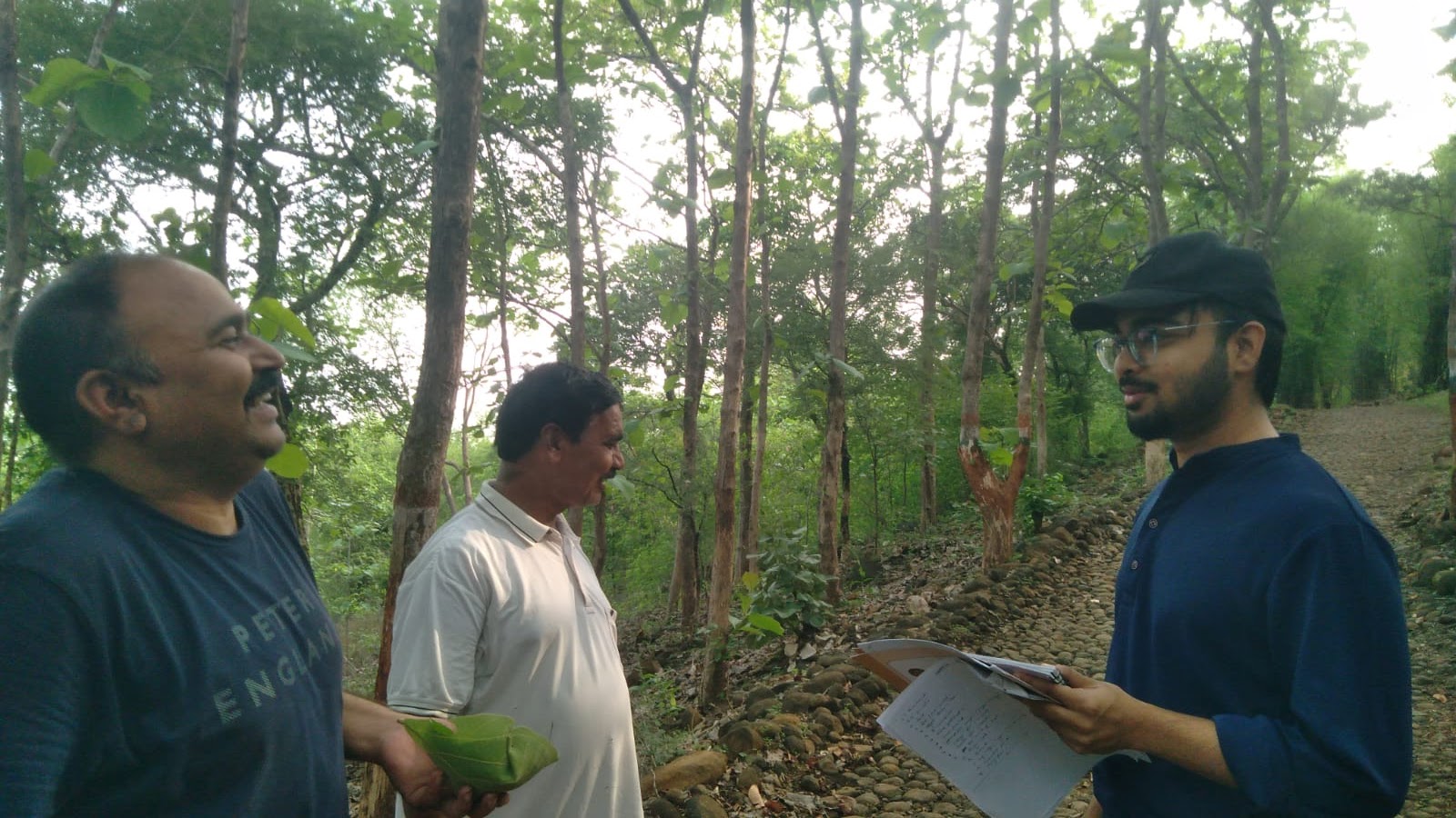 Arkraj Biswas discussing survey papers with two field workers among trees during fieldwork